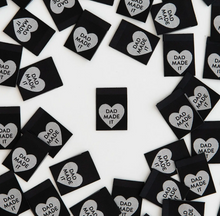 Load image into Gallery viewer, Woven label by Sarah Hearts black background with silver white heart and Dad Made It in type inside the heart for clothing garments bags costumes totes