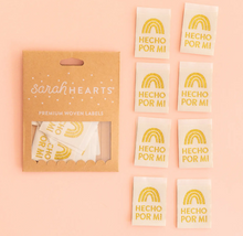 Load image into Gallery viewer, Woven Labels by Sarah Hearts white background with gold rainbow and Hecho por Mi or Made by Me in Spanish in gold for clothing garments purses tote bags quilts cotton washable