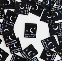 Load image into Gallery viewer, Woven center fold label by Sarah Hearts black background with fingernail moon and 2 eight point stars in white and gold dots Made Under Moonlight in white type print for garments clothing makers tote bags quilts