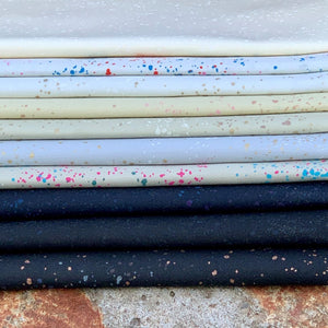 Curated fat quarter bundle of Speckled by Ruby Star Society for Moda Fabrics in shades of black gray cream white spatters of color and gold metallic are splashed across each fabric 