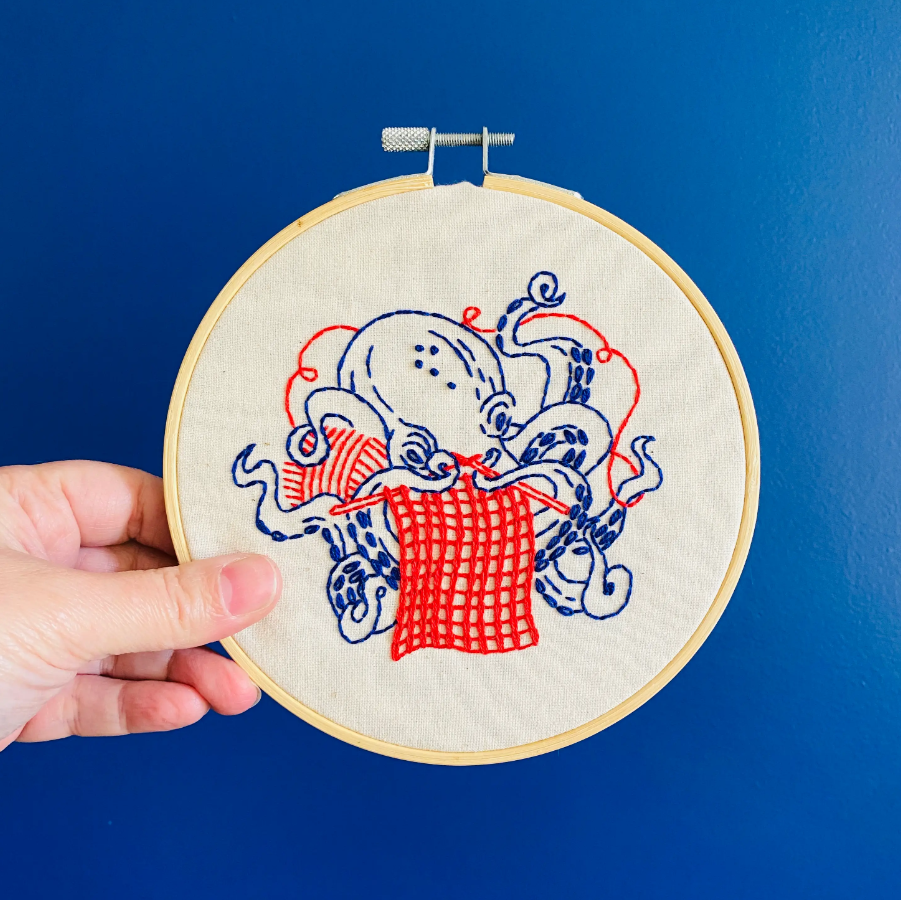 Hook Line and Tinker Embroidery KIt Blue Octopus knitting a red scarf with a ball of yarn complete kit includes thread hoop preprinted canvas needle and instructions in English and French for handwork