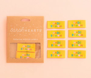 Woven end fold labels by Sarah Hearts bright yellow background with Made by Mom in rainbow colors of turquoise green orange pink with pink heart instead of an O in Mom used for clothing garments quilts costumes bags totes purses crafts